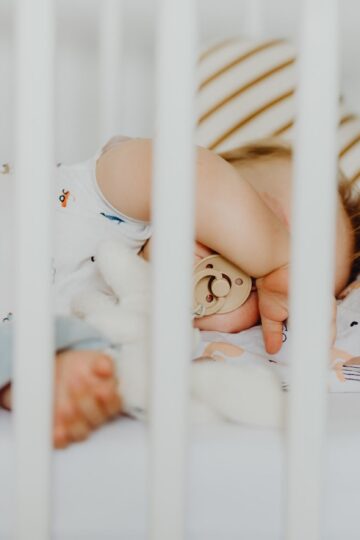A baby peacefully sleeping with a pacifier in a cozy crib with plush blankets.