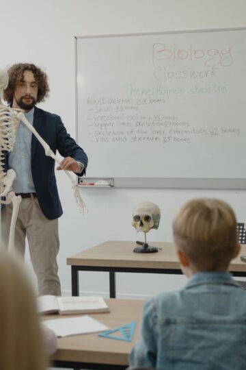 Teacher explaining human skeleton to students in a biology class with models.