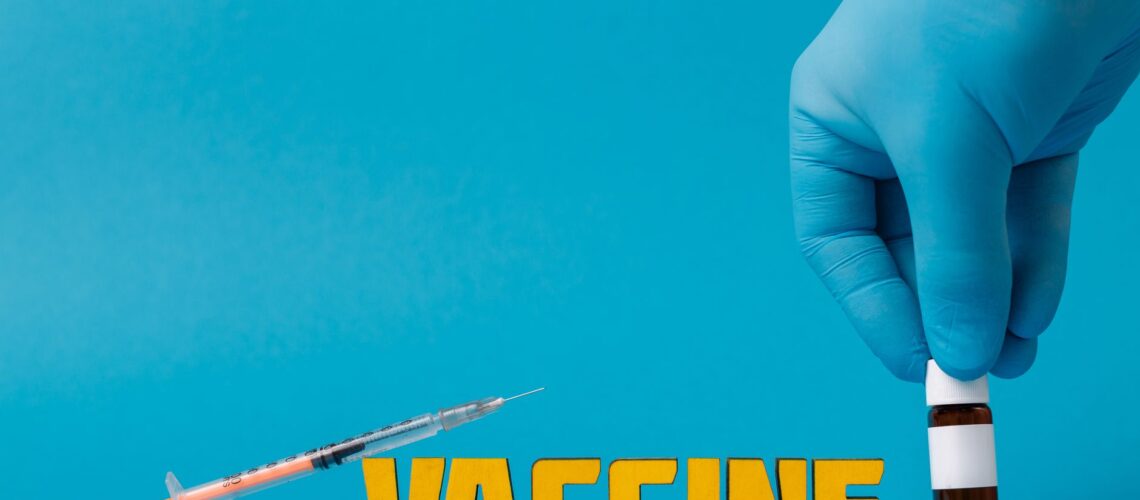 Medical concept with syringe and vaccine bottle against blue background featuring yellow text "VACCINE".