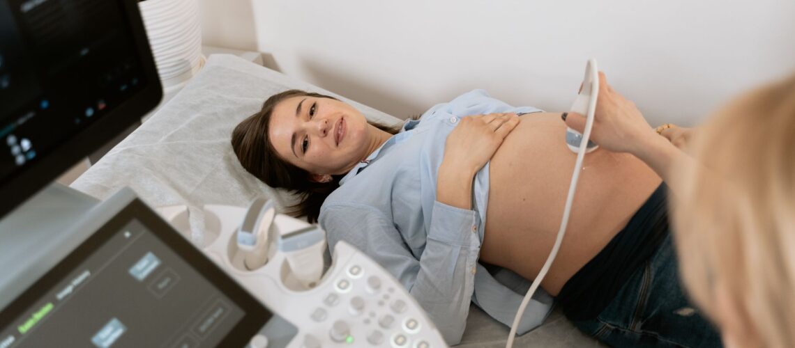 Pregnant woman undergoing an ultrasound scan, assisted by a healthcare professional in a medical clinic.