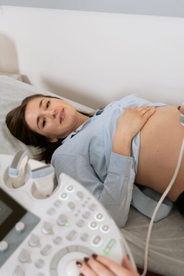 Pregnant woman undergoing an ultrasound scan, assisted by a healthcare professional in a medical clinic.