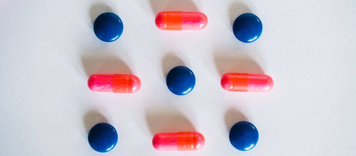 Various blue and pink pills and capsules arranged on a white background, showcasing medication.