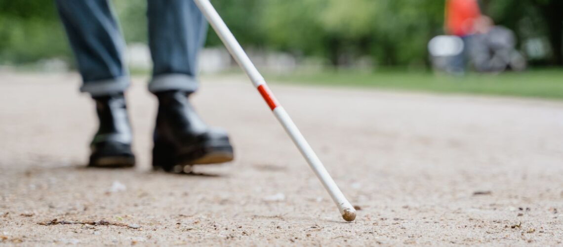 Close-up of a walking stick used by a visually impaired person in a park, symbolizing independence and mobility.