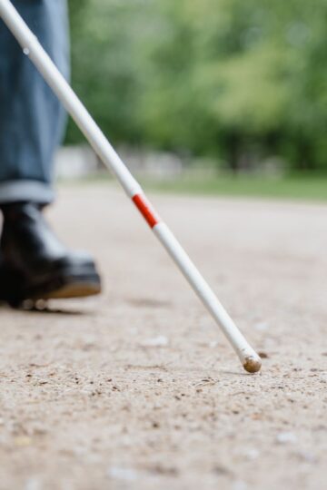 Close-up of a walking stick used by a visually impaired person in a park, symbolizing independence and mobility.