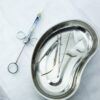 A set of sterile medical tools and syringe displayed in a kidney tray for dental or surgical use.