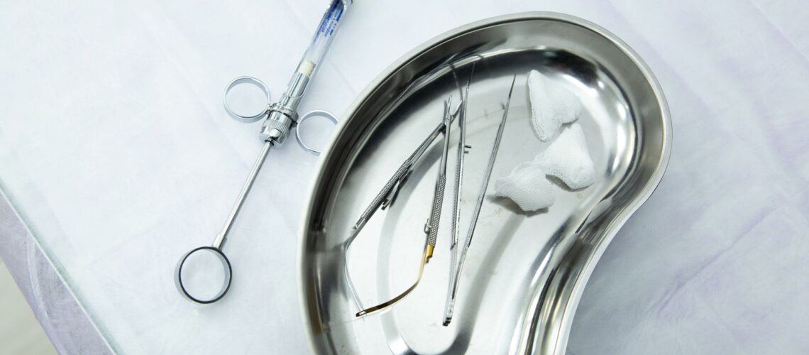 A set of sterile medical tools and syringe displayed in a kidney tray for dental or surgical use.