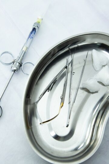 A set of sterile medical tools and syringe displayed in a kidney tray for dental or surgical use.