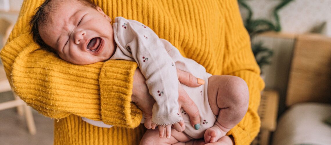 A mother gently holds a crying baby in her arms, providing warmth and comfort indoors.