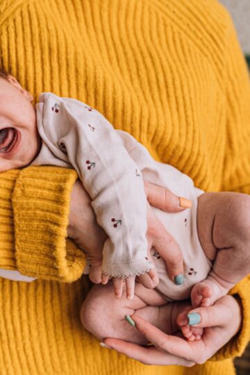 A mother gently holds a crying baby in her arms, providing warmth and comfort indoors.