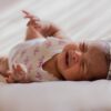 A close-up of a crying baby wearing a headband, lying on a soft bed indoors.