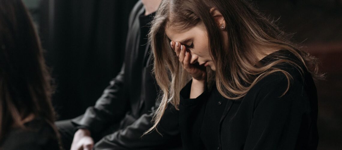 A woman in black clothing expresses sorrow at a funeral, reflecting on loss.