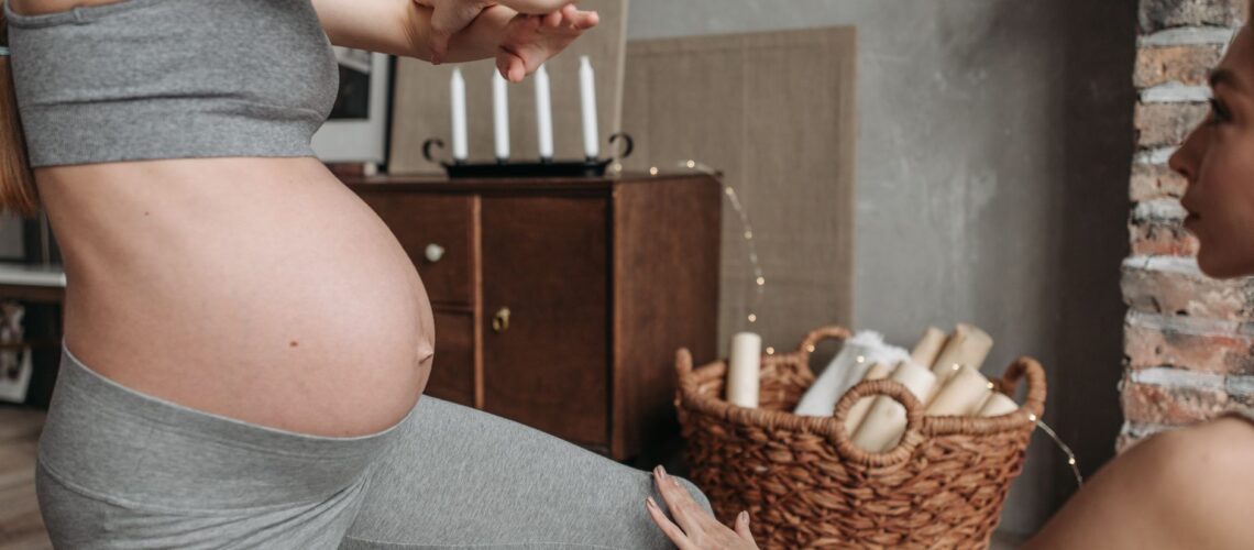 Pregnant woman doing yoga indoors with instructor assistance, emphasizing fitness and well-being.