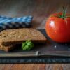 A rustic still life featuring fresh tomato and whole grain bread on a slate board.