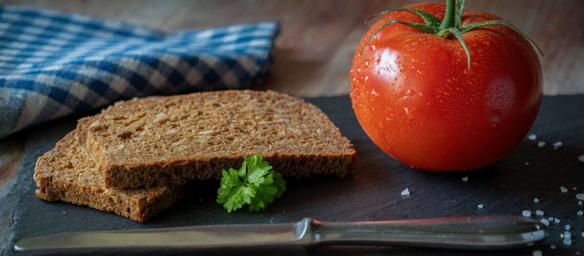 A rustic still life featuring fresh tomato and whole grain bread on a slate board.