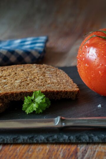 A rustic still life featuring fresh tomato and whole grain bread on a slate board.