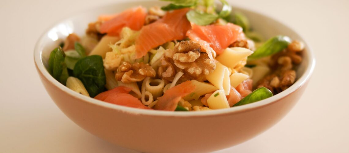 Delicious pasta salad featuring smoked salmon, walnuts, and fresh greens in a ceramic bowl.