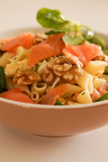 Delicious pasta salad featuring smoked salmon, walnuts, and fresh greens in a ceramic bowl.