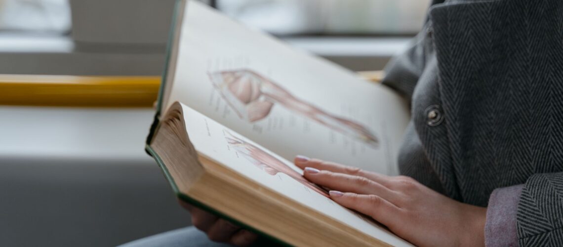 Close-up of hands holding an anatomy book, studying human muscles in a train.
