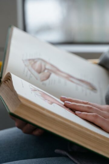 Close-up of hands holding an anatomy book, studying human muscles in a train.