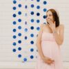 A surprised pregnant woman in a pink dress at a gender reveal party indoors with blue decorations.