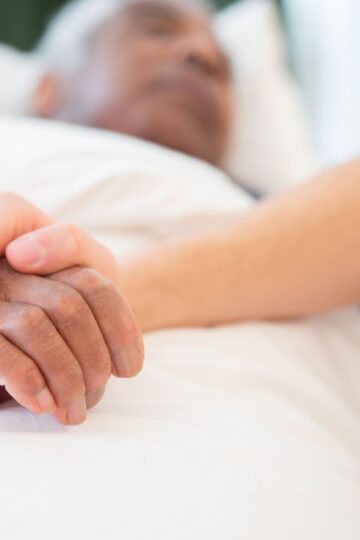 A comforting gesture as a hand holds another in a hospital setting, symbolizing care and support.
