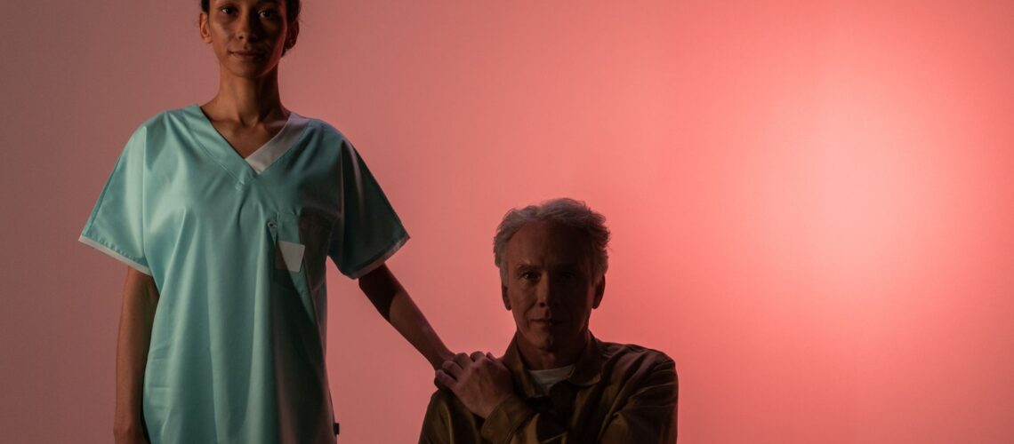 Nurse comforts elderly patient, symbolizing compassion and support. Studio setting with pink background.