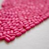 Bright pink pills arranged on a white surface, emphasizing medication details.