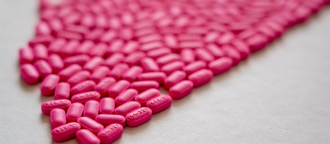 Bright pink pills arranged on a white surface, emphasizing medication details.