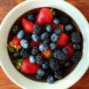 A vibrant assortment of strawberries, blackberries, and blueberries in a bowl on a wooden surface.