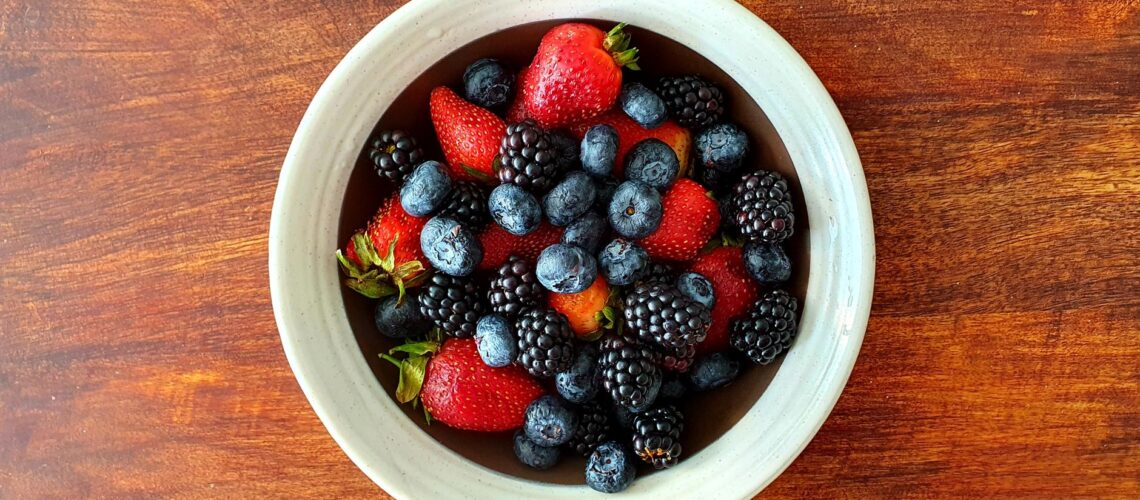 A vibrant assortment of strawberries, blackberries, and blueberries in a bowl on a wooden surface.