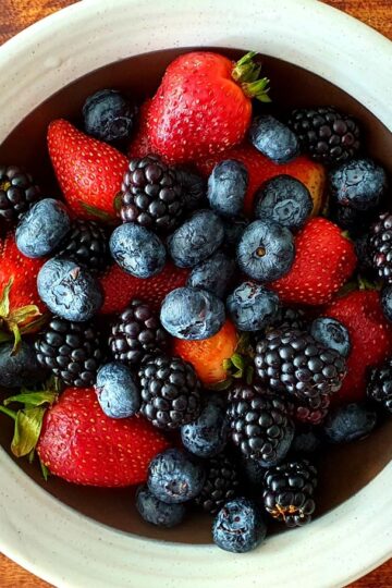 A vibrant assortment of strawberries, blackberries, and blueberries in a bowl on a wooden surface.