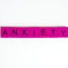 Pink Scrabble tiles spelling 'anxiety' on a white surface. Concept of mental health.