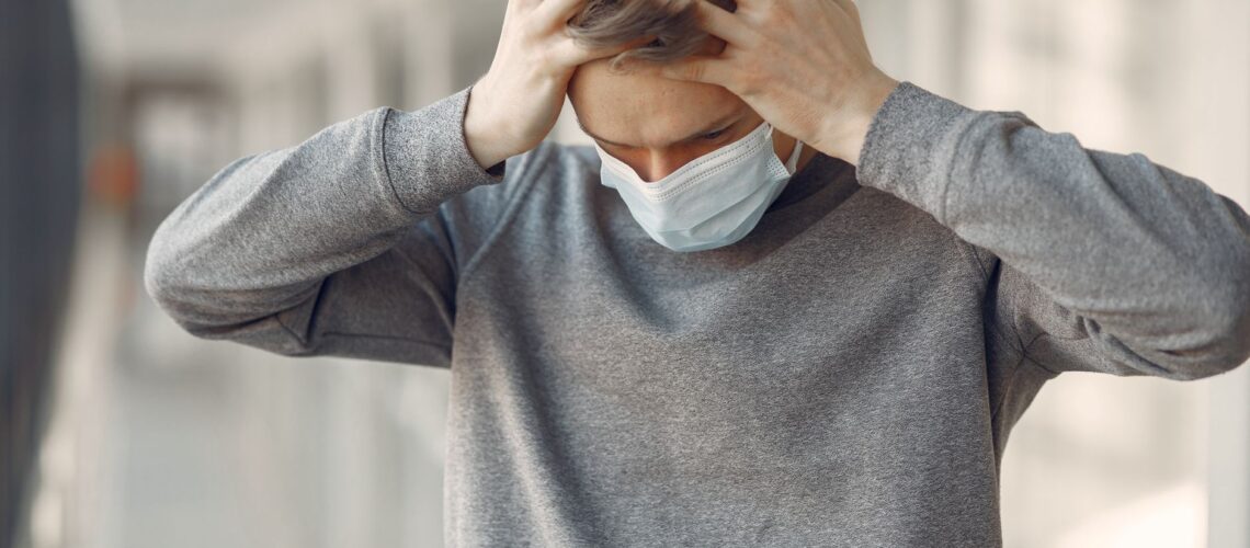 Adult male wearing a face mask, appearing stressed and worried while standing indoors.