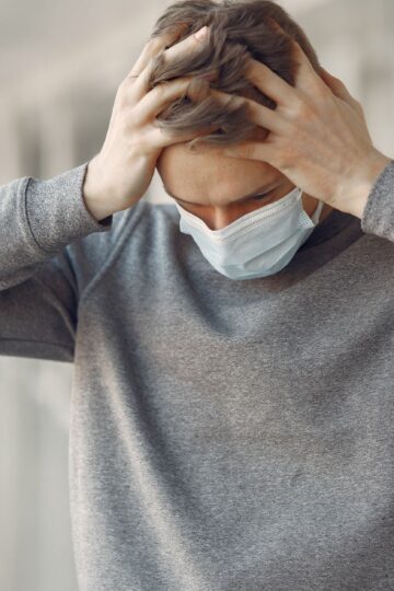 Adult male wearing a face mask, appearing stressed and worried while standing indoors.