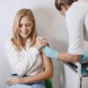 Blonde woman receives vaccination from healthcare professional indoor.