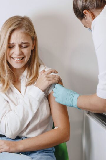 Blonde woman receives vaccination from healthcare professional indoor.