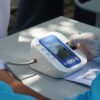 Healthcare worker checking patient's blood pressure with a digital device outdoors.