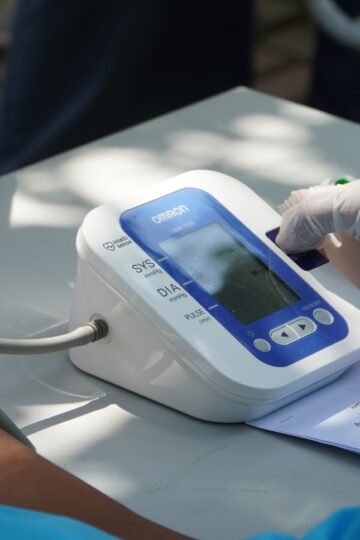 Healthcare worker checking patient's blood pressure with a digital device outdoors.