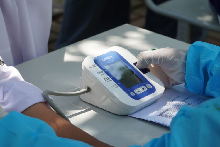 Healthcare worker checking patient's blood pressure with a digital device outdoors.