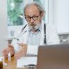 An elderly doctor in a white coat conducting an online medical consultation, focusing attentively.