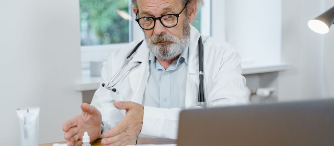 An elderly doctor in a white coat conducting an online medical consultation, focusing attentively.