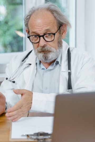 An elderly doctor in a white coat conducting an online medical consultation, focusing attentively.
