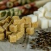 Close-up of brown sugar cubes, white sugar cubes, and tea leaves on a wooden surface.