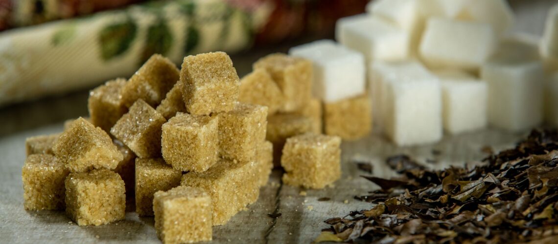Close-up of brown sugar cubes, white sugar cubes, and tea leaves on a wooden surface.