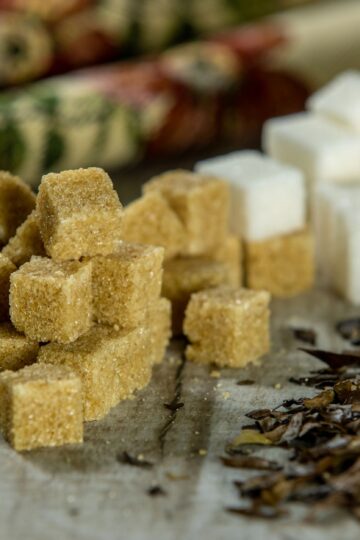 Close-up of brown sugar cubes, white sugar cubes, and tea leaves on a wooden surface.