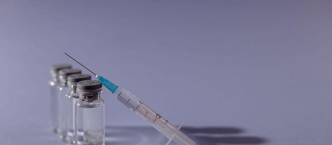 Syringe and vaccine vials arranged on gray surface, symbolizing healthcare and immunization.