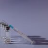 Syringe and vaccine vials arranged on gray surface, symbolizing healthcare and immunization.