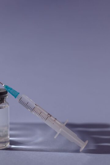 Syringe and vaccine vials arranged on gray surface, symbolizing healthcare and immunization.