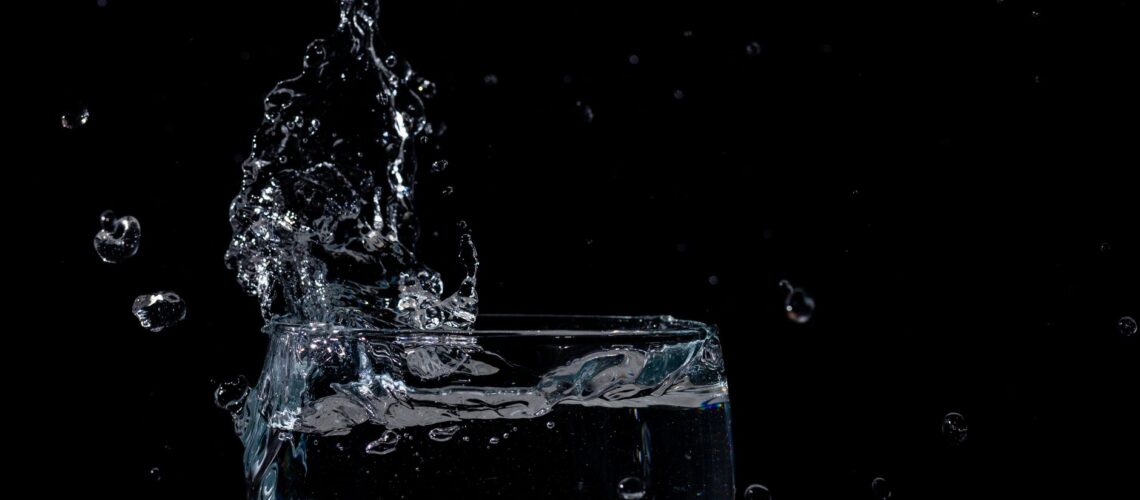 Close-up of water splashing in a glass against a black background.