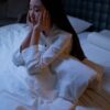 An Asian woman in bed at night, experiencing insomnia and loneliness, deep in thought.